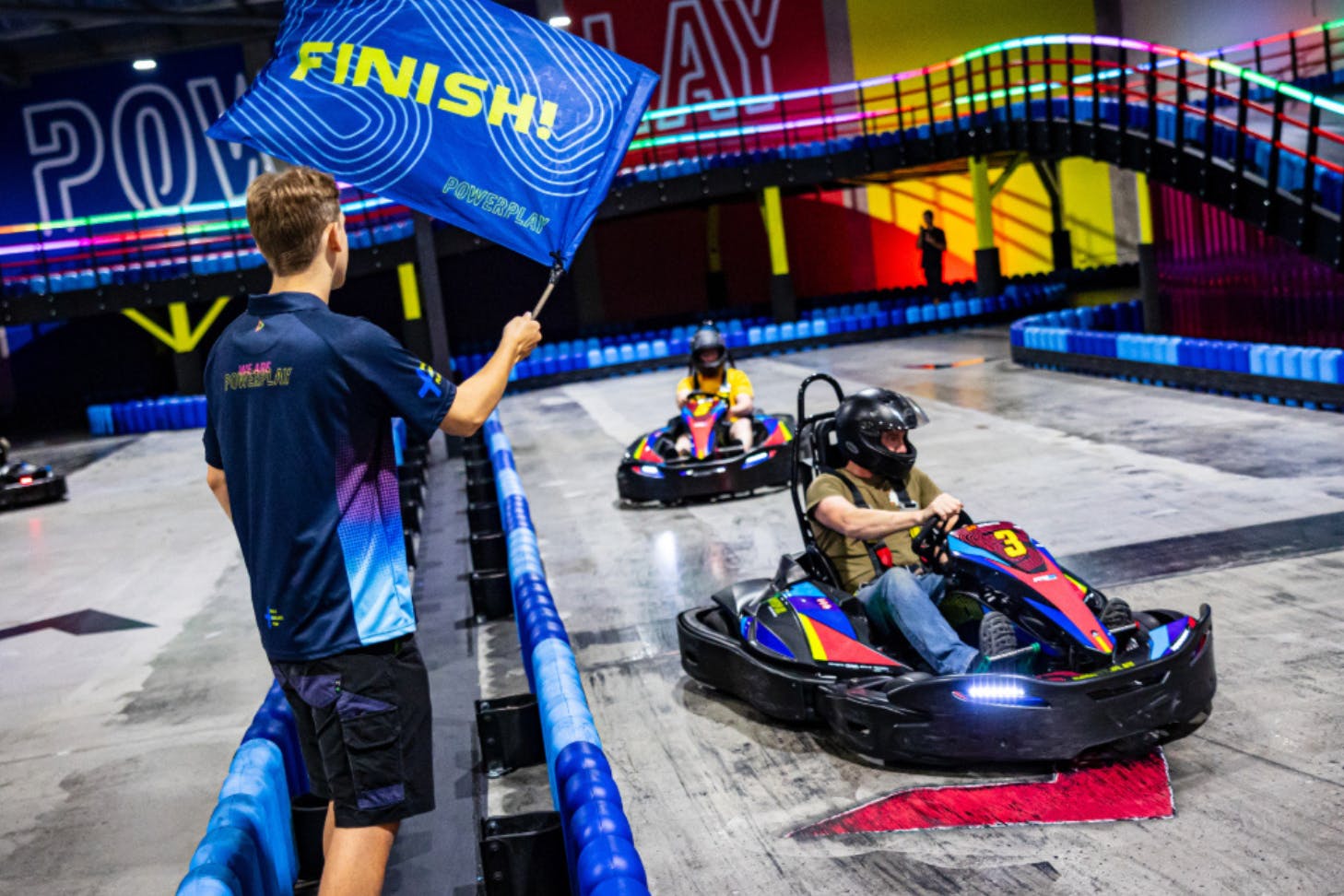 A go-kart rider crosses the finish line to a waving flag at Power Play